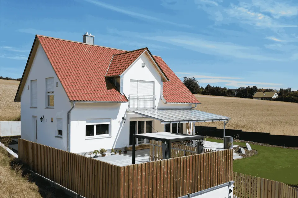 Einfamilienhaus mit angelegter Terrasse, Rasenfläche und Zaun aus der Drohnenperspektive